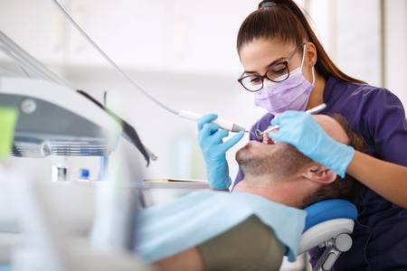 96533642 female dentist drilling tooth to male patient in dental chair